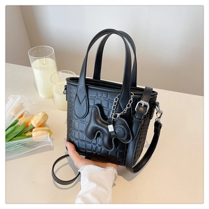 Detail of black crocodile texture mini tote bag with stylish dog charm on a clean surface