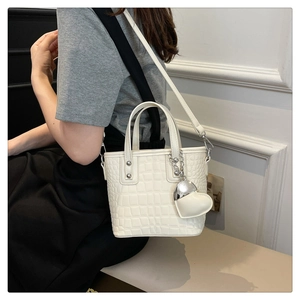 Detailed view of cream crocodile-embossed bucket bag with heart pendant and strap