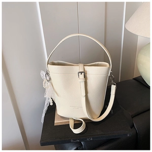 Dettaglio borsa a secchiello in pelle beige martellata con ciondolo in pizzo e perle