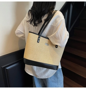 Detail of woven straw tote bag with black leather trim and metal logo on a model