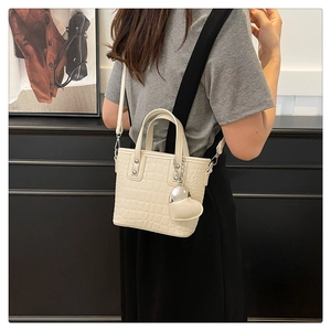 Detail of off-white crocodile embossed bucket bag with a heart pendant shown on a model