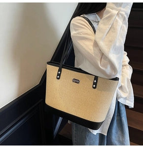 Detail of woven straw tote bag featuring black leather trim and silver metal logo