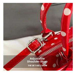 Détail de la boucle en métal et du zip sur le sac rouge à pois en cuir verni
