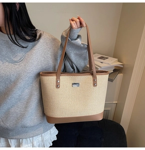Detail of woven tote bag with brown leather trim and metal logo plate on a shoulder strap