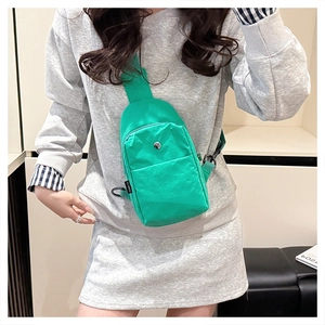Model wearing a bright green nylon crossbody bag with black metal zippers and strap