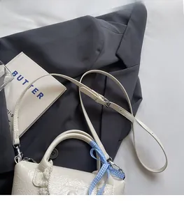 Detail of off-white pleated bag with blue ribbon and adjustable shoulder strap feature