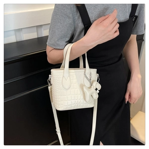 Detail of white crocodile pattern bag with a cute dog pendant and adjustable strap