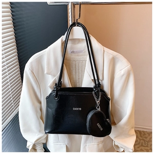 Détail du sac seau en cuir noir avec pendentif cœur sur fond de blazer blanc élégant