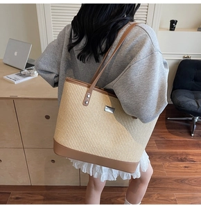 Close-up of woven tote bag with brown faux leather straps and metal logo detail