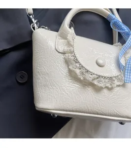 Detail of white glossy bucket bag with lace trim and blue checkered ribbon accent