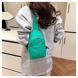 Detail of green nylon crossbody chest bag with round metal logo shown on model back