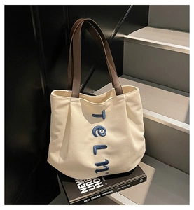 Close-up of beige canvas tote with brown leather handles and blue artistic lettering