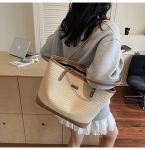 Detail of woven straw tote bag with brown leather trim and metal logo on the front