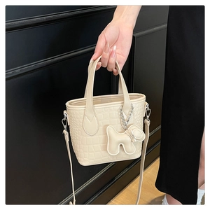 Detail of cream mini bucket bag with crocodile texture and cute puppy charm accessory