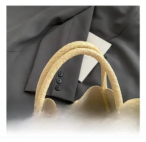 Détail de l'anse du sac seau tressé crème avec fermeture éclair sur blazer gris foncé