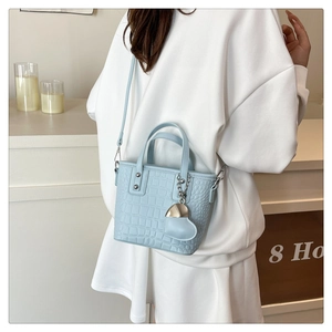 Detail of light blue croc-embossed bucket bag with heart charm and silver rivets