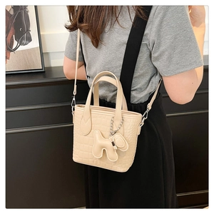 Detail of cream faux leather bucket bag with crocodile texture and cute dog charm