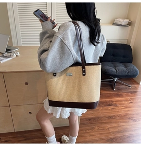 Detail view of a large woven tote bag with brown leather handles in a commuter office setting