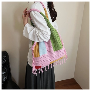 Model wearing a large colorful patchwork knit tote bag with bohemian tassel details