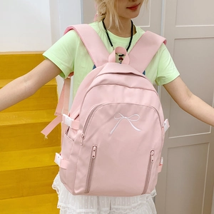 Détail d'un sac à dos rose en tissu avec broderie nœud blanc et sangles réglables latérales