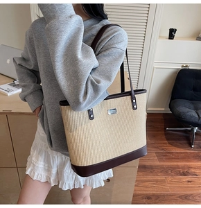 Detail of woven straw tote bag with brown leather handles and silver metal logo plate