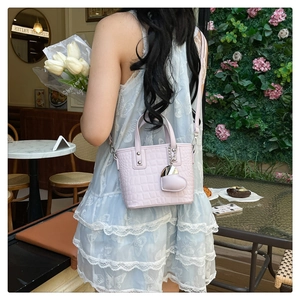 Detail of light purple crocodile embossed tote bag with heart charm in a cafe setting
