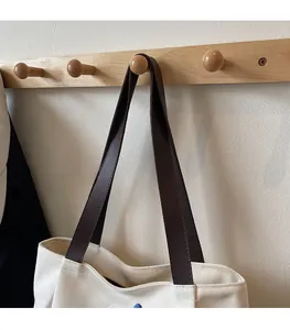 Detailed view of durable brown leather shoulder straps on a canvas tote bag