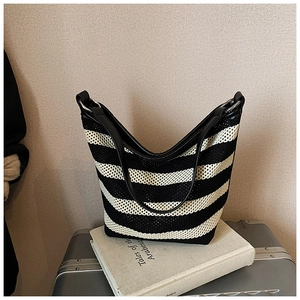 Detail of black and white striped knit tote bag with leather straps on a silver suitcase