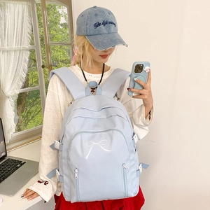 Détail d'un sac à dos bleu clair avec motif de nœud blanc et plusieurs poches zippées pratiques
