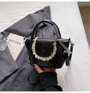 Detail of black glossy bucket bag featuring white lace trim and checkered ribbon handle
