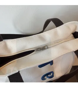 Detail of silver metal zipper closure and embroidered blue letters on canvas tote bag