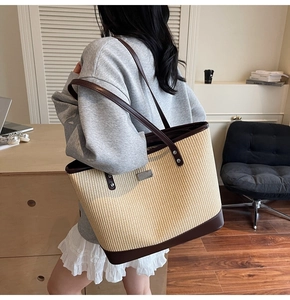 Detail of woven tote bag with brown leather trim and metal logo plate worn by model