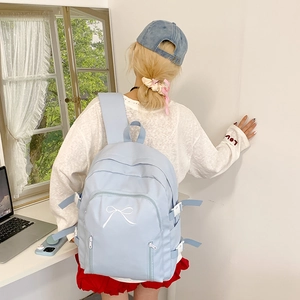 Détail du sac à dos bleu clair avec broderie nœud blanc et sangles à boucle latérale