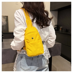 Detail of a bright yellow nylon chest bag showing the silver button pocket and side logo