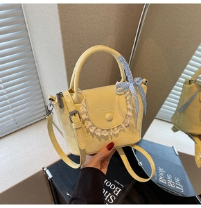 Detail of cream crossbody bucket bag with delicate white lace and checkered ribbon bow