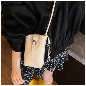 Detail of a beige bucket phone bag with silver ring hardware on a crossbody strap