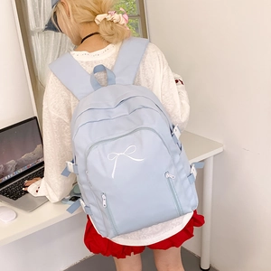 Détail du sac à dos bleu clair avec broderie de nœud blanc et poche zippée