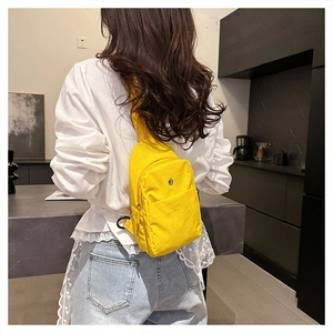 Detail view of a bright yellow nylon chest bag worn by a model in a modern kitchen setting