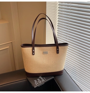Detail of woven tote bag with dark brown leather handles and silver metal logo plate