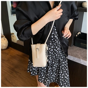 Detail of minimalist cream-white crossbody bucket bag showing metal clasp and shoulder strap