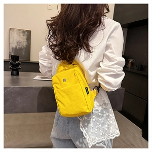 Rear view of a bright yellow canvas chest bag worn by a model in a modern interior