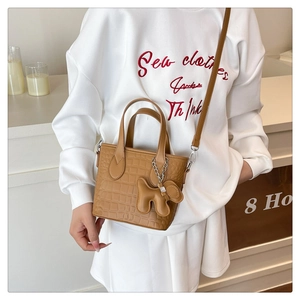 Detail of caramel crocodile pattern bucket bag with cute dog charm on white sweater