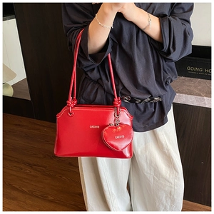 Détail d'un sac à bandoulière en cuir rouge brillant avec pendentif coeur et logo chic