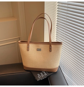Detail of woven straw tote bag with brown leather handles and central metal plate