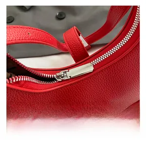 Detailed macro view of silver hardware zipper and buckle on a red lychee leather handbag