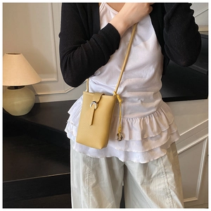 Close-up of a yellow textured leather bucket bag with silver horse-bit buckle on a model