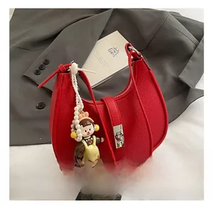 Detail of red pebbled leather half-moon bag with silver buckle and pearl doll charm