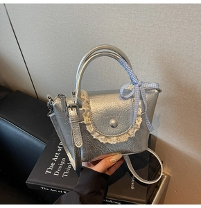 Detail of silver bucket bag with pleated texture, lace trim, and blue plaid bow ribbon