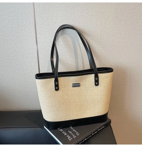 Close-up of beige straw tote bag featuring black leather trim and metal logo detail