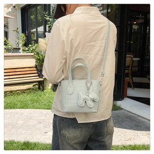 Close-up of light blue crocodile embossed texture handbag with cute puppy charm accessory